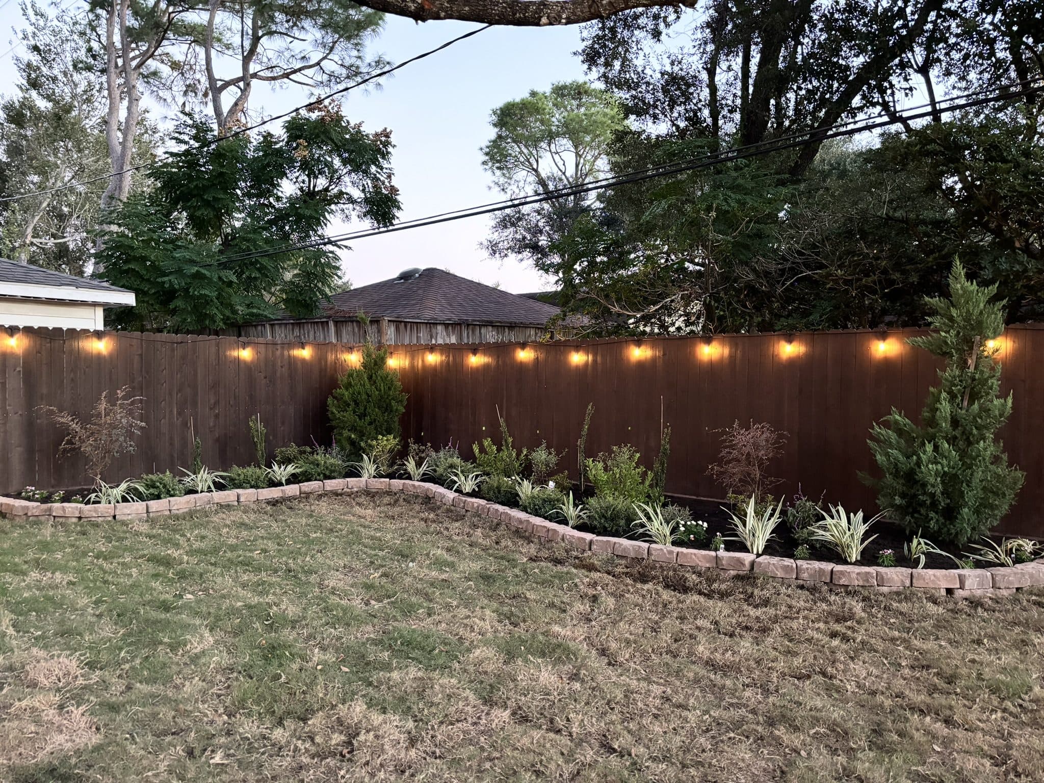 A new stone-edged perimeter border planted with evergreens and grasses beneath festoon lighting.