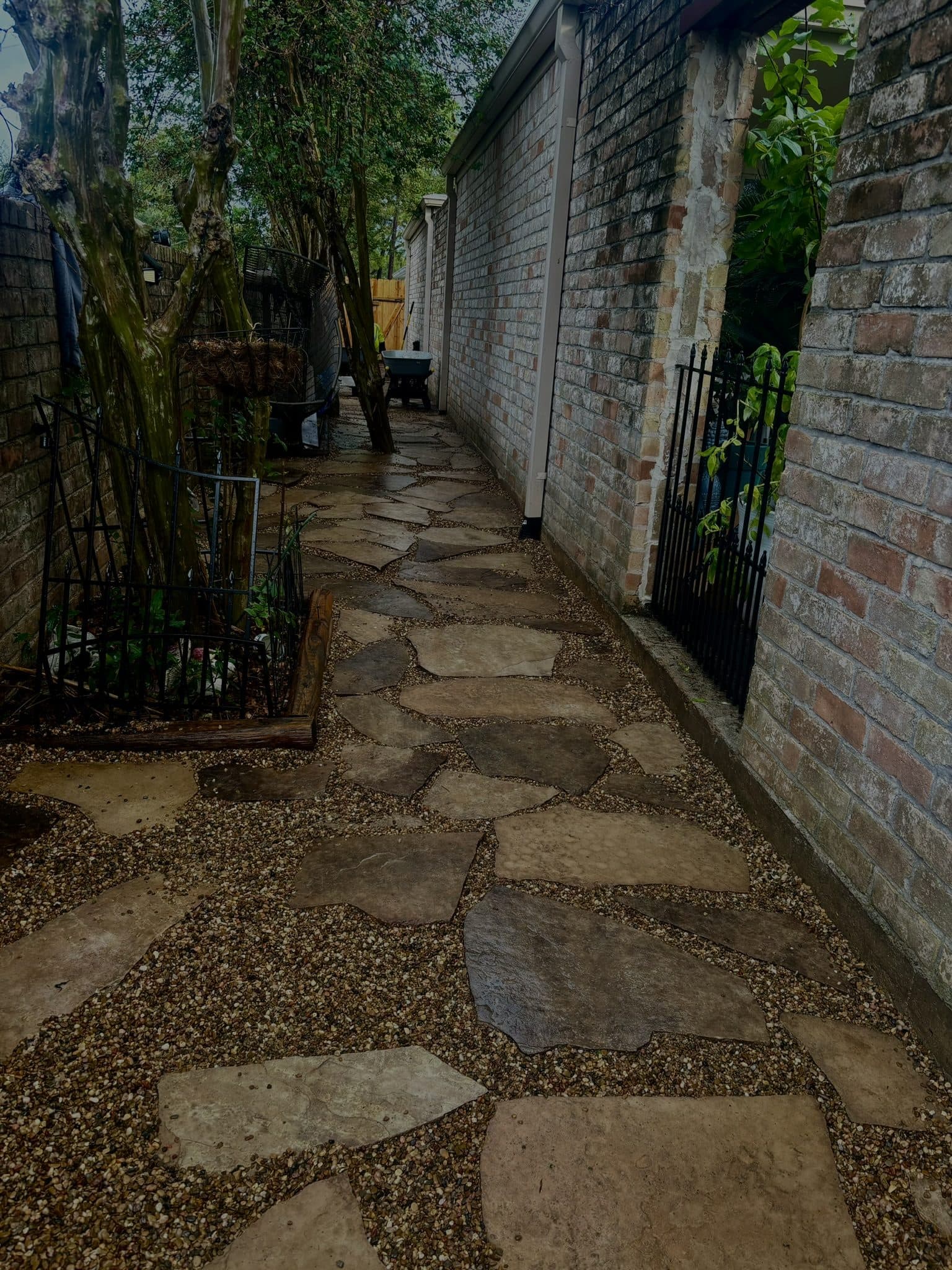 Irregular flagstone set in gravel forming a narrow side passage between walls.