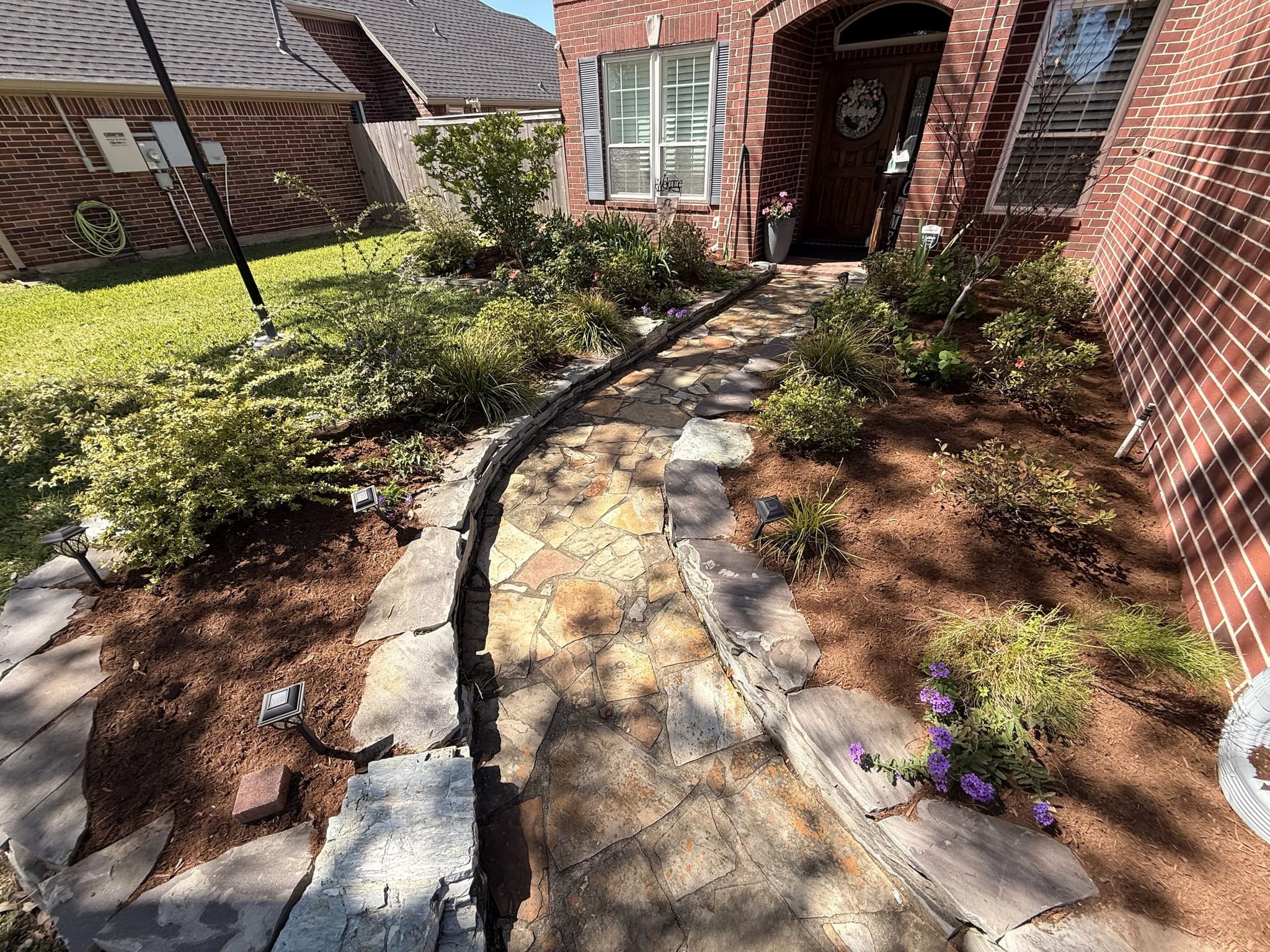 A flagstone entry walkway rebuilt with steel edging and fresh planting beds against a brick home.