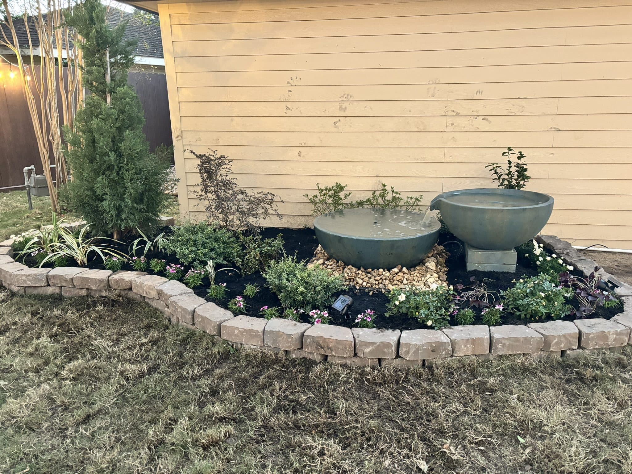 A stone-edged bed built around cast fountain bowls with layered evergreen planting.