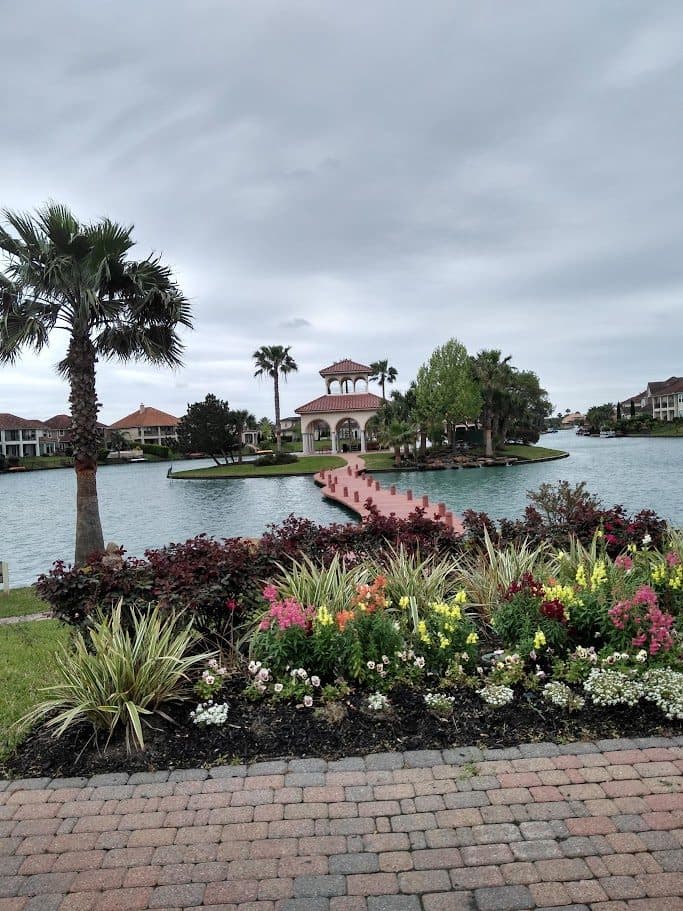 A wide flowering border with palms and seasonal colour running along a lakefront brick paver walk.