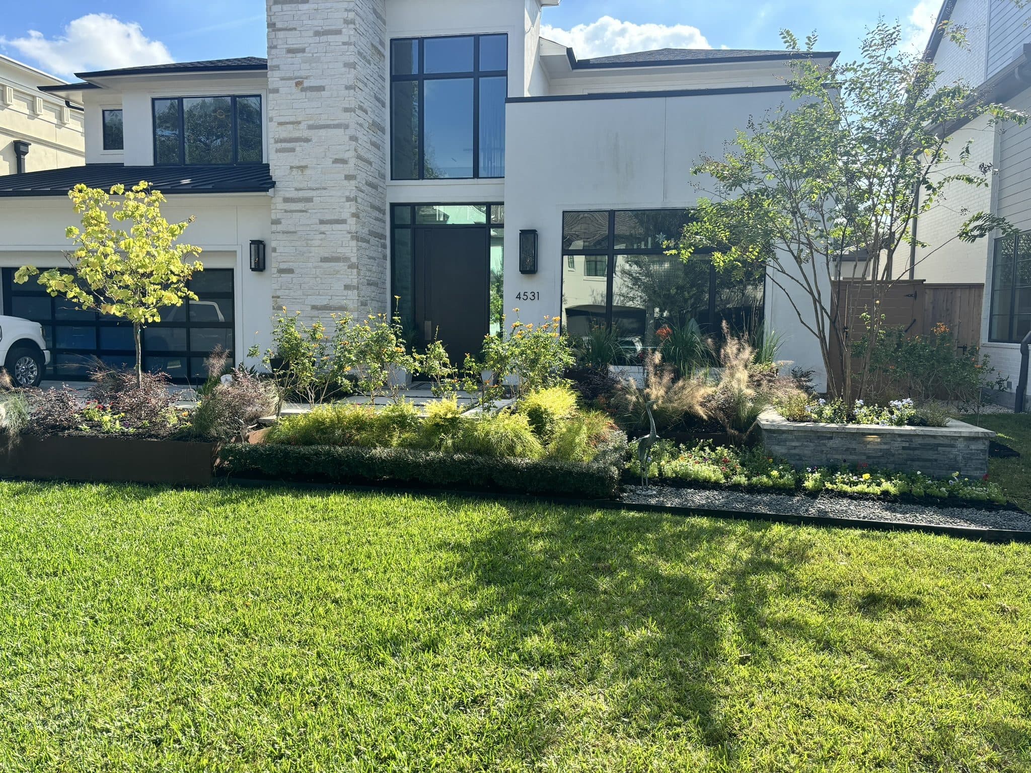 Freshly installed layered planting bed and manicured St. Augustine lawn fronting a modern white Houston home.