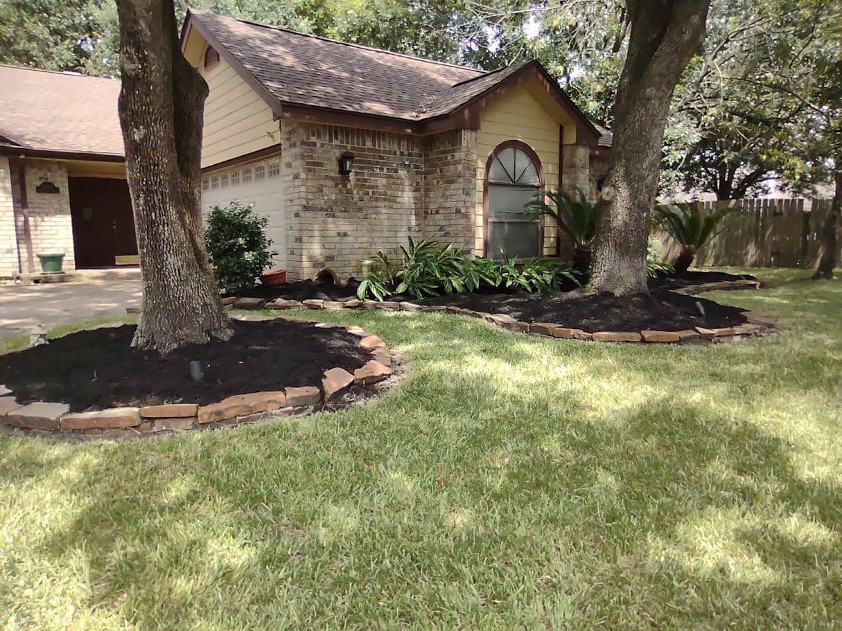 Curved beds cut and mulched beneath mature oaks at a stone-fronted Houston home.