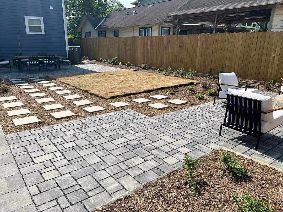 A grey paver patio being laid alongside fresh sod and stepping stones in a Houston backyard.