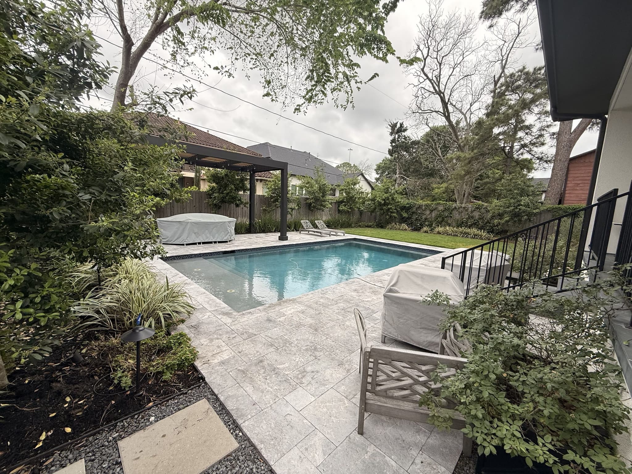 A paver pool deck with pergola and planting beds in a mature Houston backyard.