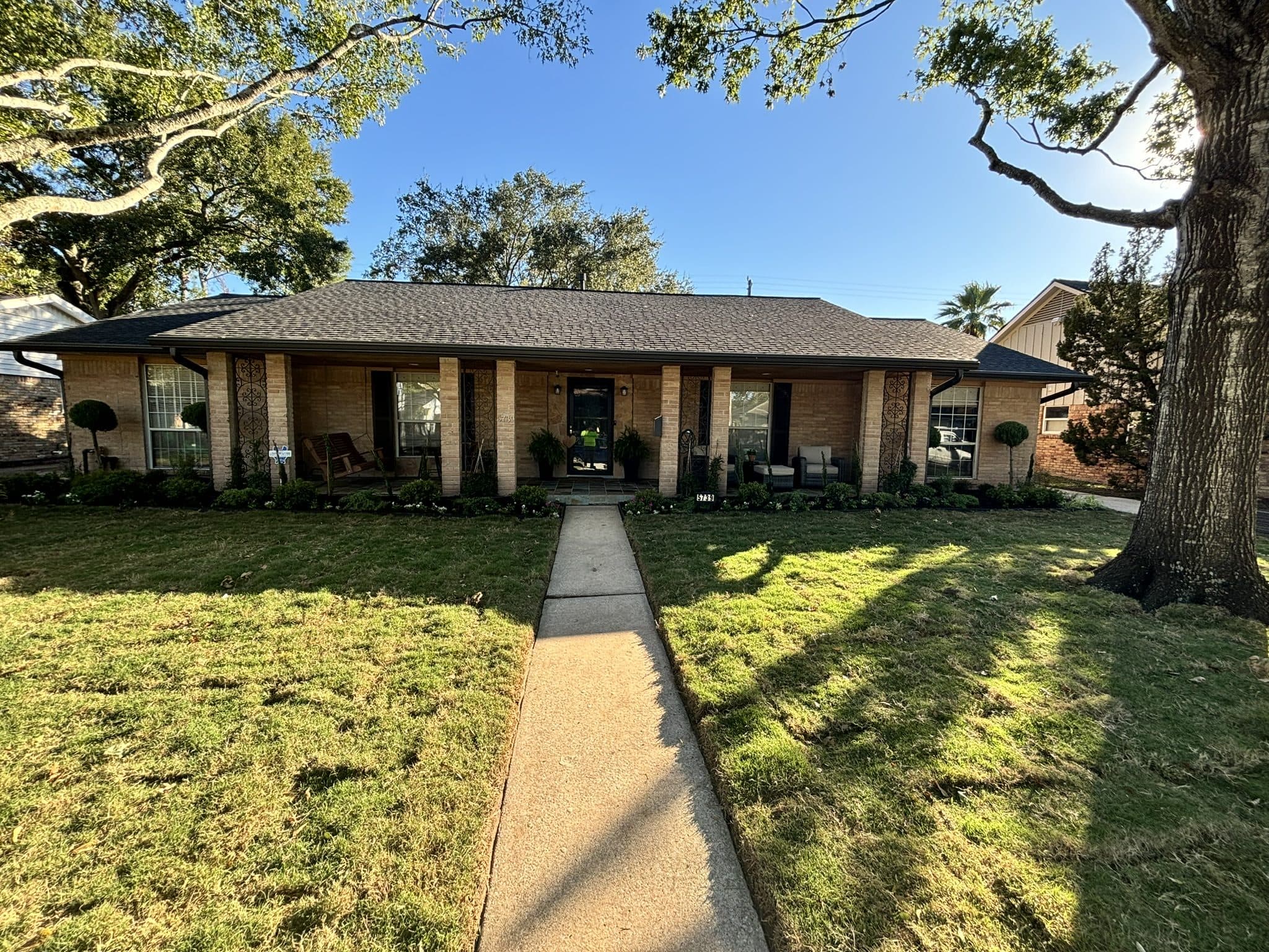 A mid-century ranch frontage with an exposed-aggregate walk and maintained lawn under mature oaks.