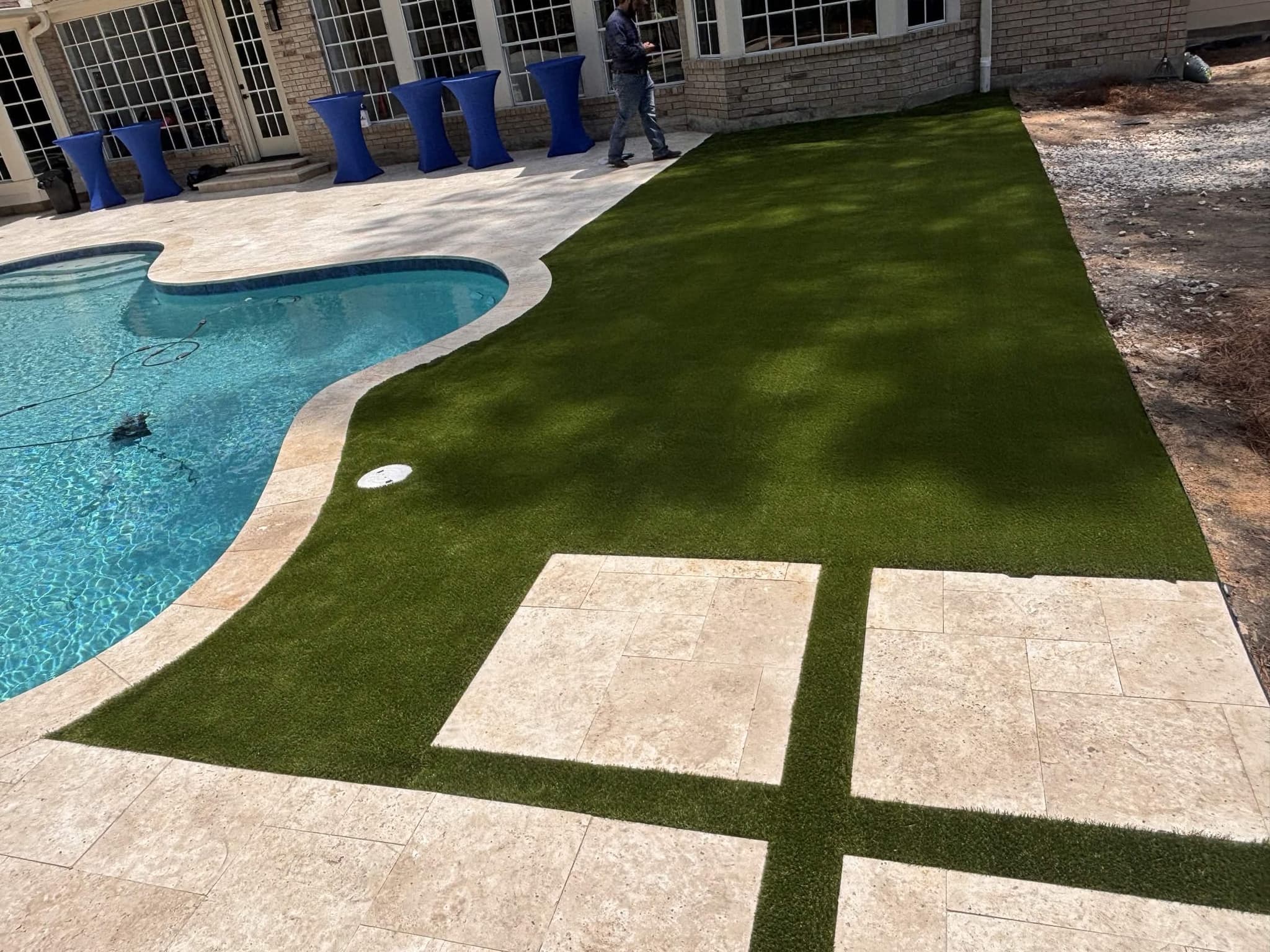 Artificial turf lawn inlaid with travertine pavers, wrapping a curved swimming pool.