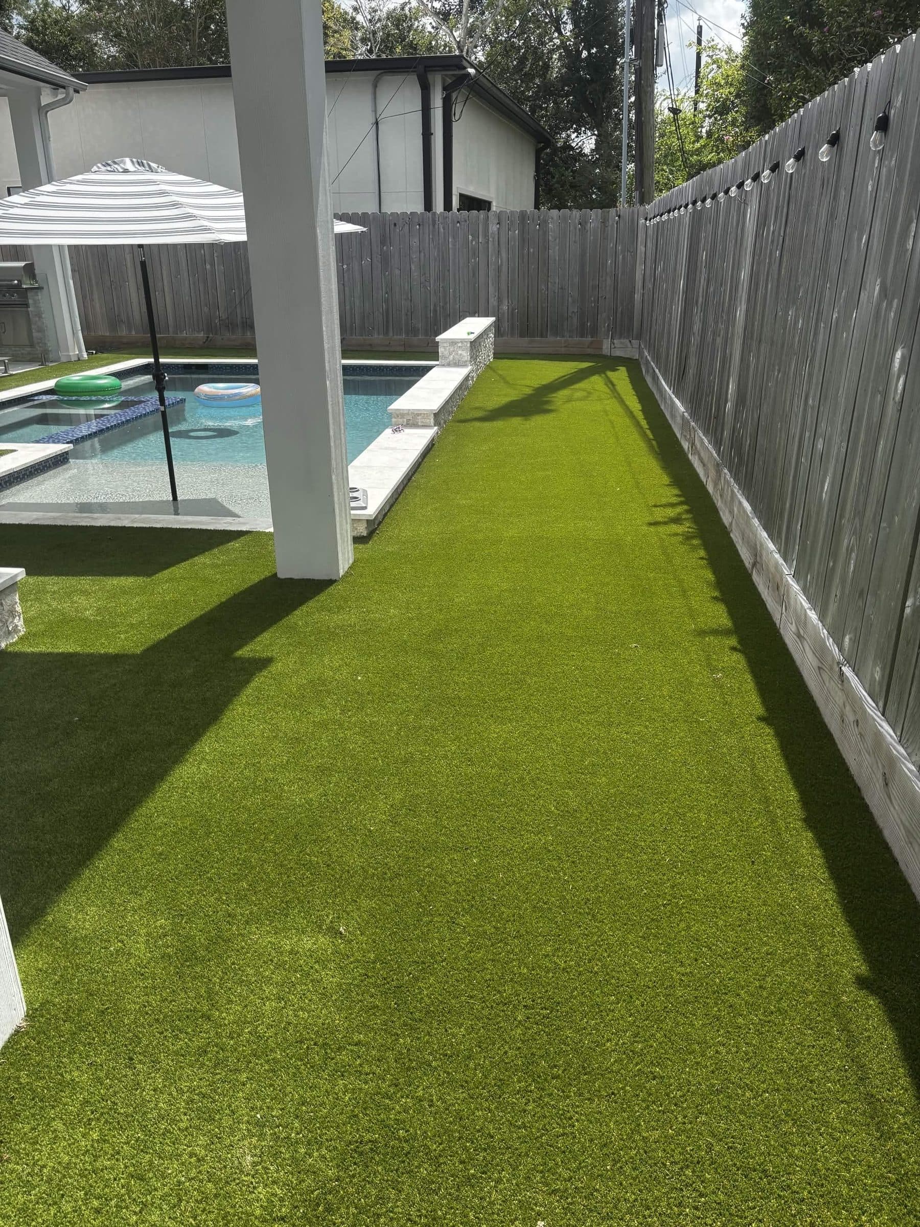 A narrow side yard converted to artificial turf beside a pool and covered patio.