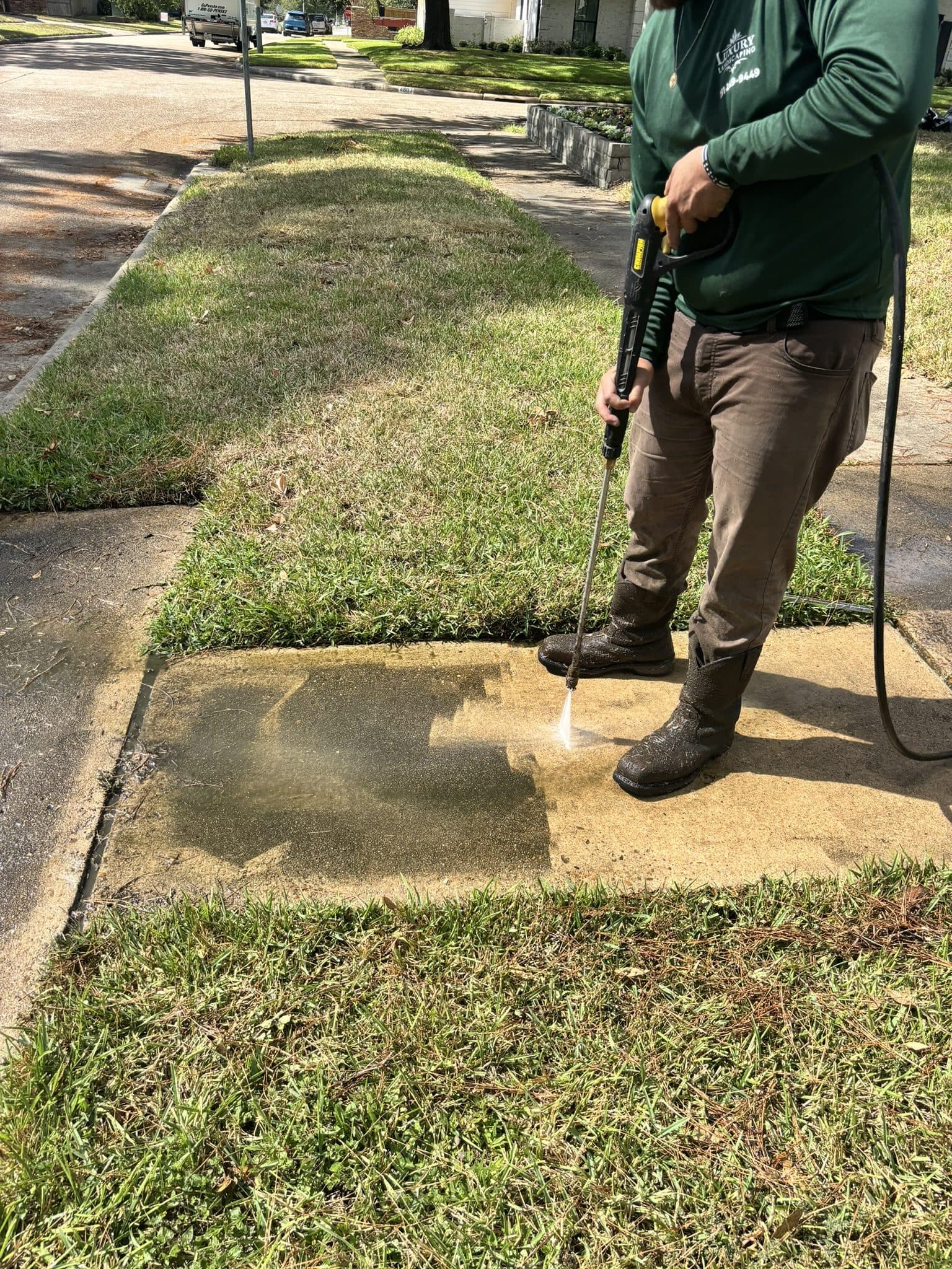 A concrete walkway being pressure washed, with the cleaned surface clearly separated from the untreated section.