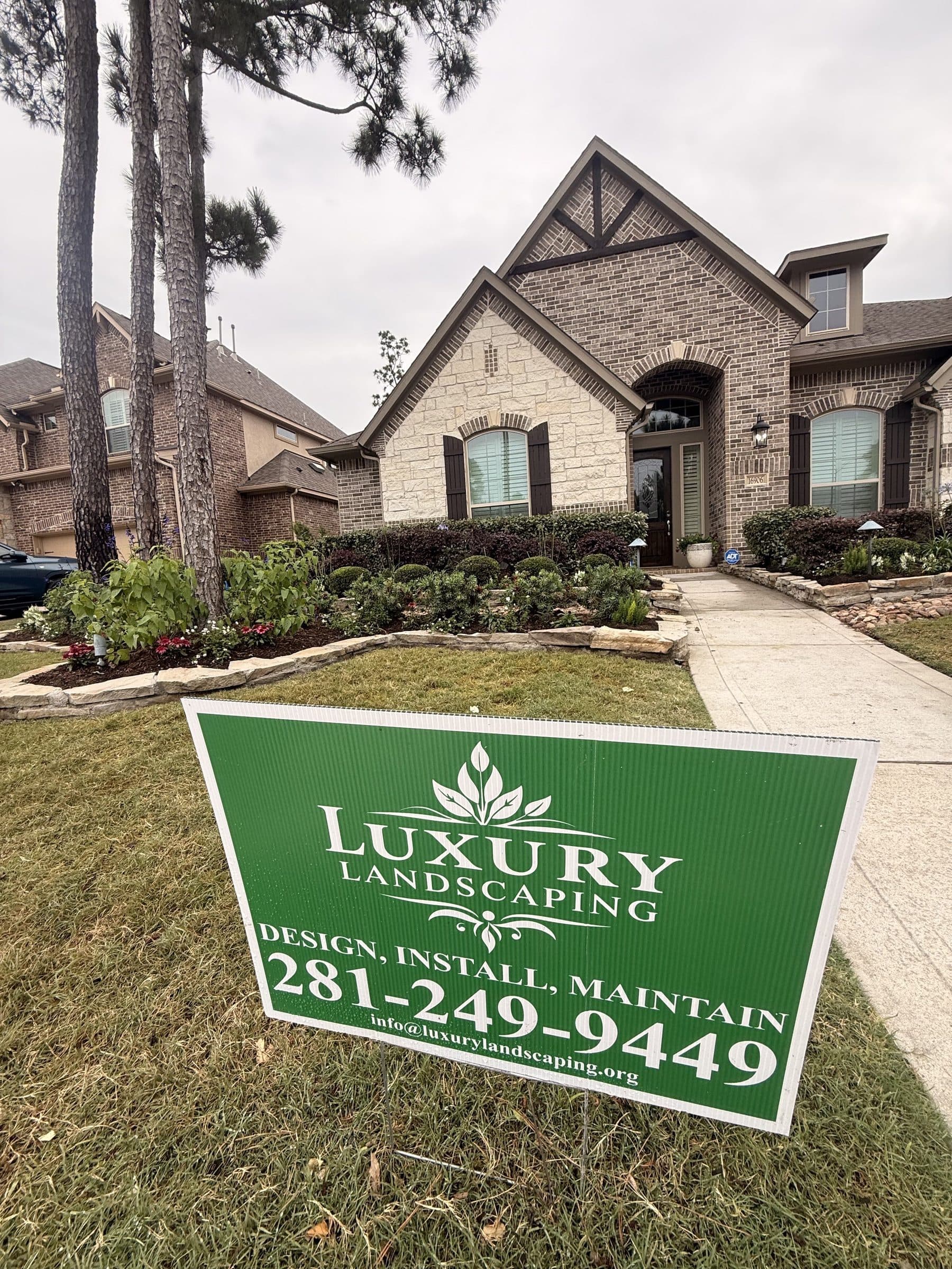 A Luxury Landscaping yard sign — design, install, maintain — staked in a completed front lawn.