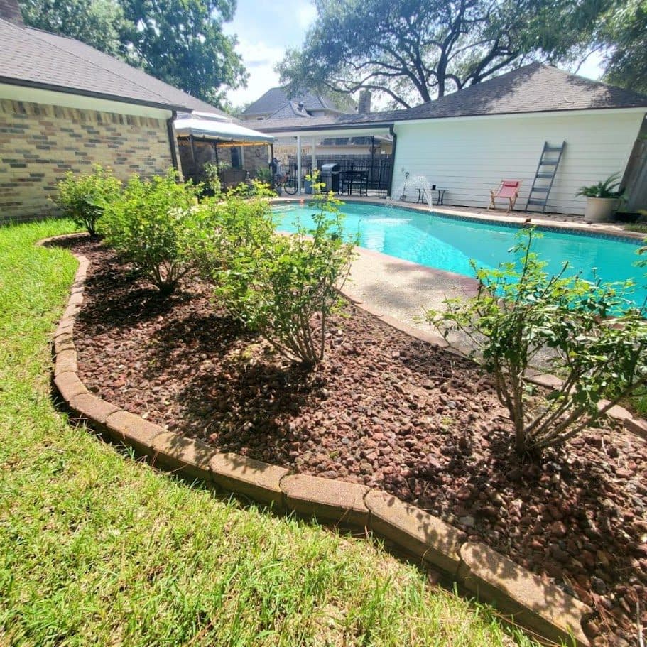A curved stone-edged border planted with shrubs, wrapping the pool deck.