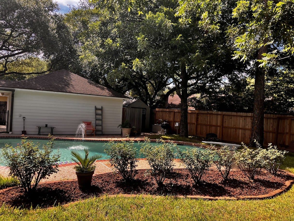 A rebuilt curved planting bed with fresh mulch and shrubs framing a backyard pool.